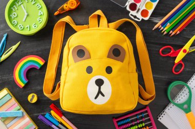 Genç öğrenciler için öğrenme sevincine bu yaratıcı üst görünüm enstantane yoluyla dalın: sarı sırt çantasının etrafında karatahta izole edilmiş arka plana karşı canlı bir çocuk kırtasiyesi derlemesi