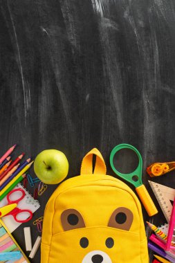 Eğitim dünyasını, sarı sırt çantası ve okul malzemelerinin izole edilmiş karatahta arka planda yer aldığı bu dikey fotoğraf ile araştırın. Metin veya reklam için kopyalama alanını kullan