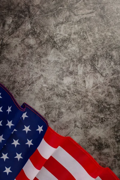 Festive mood of the public holiday: An evocative overhead vertical composition displaying the American flag on a grunge textured grey concrete backdrop. Ideal for advertisements or text placement