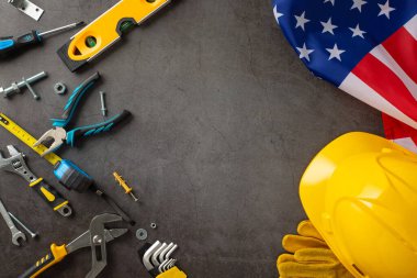 Amerikan İşçi Bayramı 'nda inşaat işçilerinin katkılarını anmak için. Bayrak, miğfer, eldiven ve grunge üzerine inşa araçları üzerinde resim telif alanı reklam veya metin için ideal gri beton
