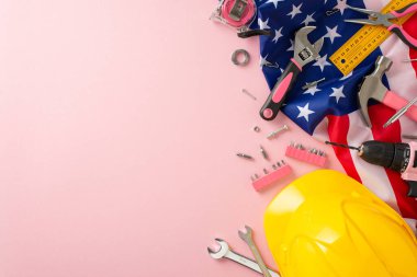 Amerikan İşçi Bayramı 'nda kadın işçilerin anısına. Yüksek açılı fotoğraf, Amerikan bayrağı ve inşaat araçlarıyla pembe bir arkaplan sergiliyor, reklamlar veya metin yerleştirmeleri için kopyalama alanı sağlıyor