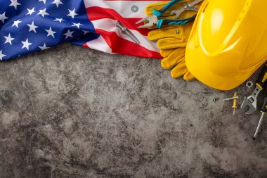 İnşaat işçilerinin yorulmak bilmeyen çabalarını İşçi Bayramı 'nda kutluyoruz. Yukarıdan aşağıya görüntü gösteren bayrak, kask, eldiven ve grunge desenli gri beton üzerindeki aletler. Reklamlar veya metinler için kopyalama alanı