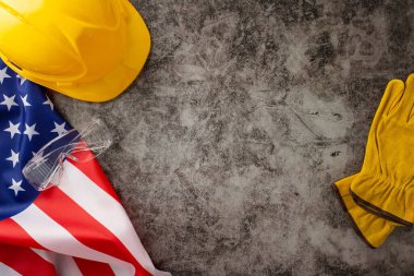 Amerikan İşçi Bayramı 'nda inşaat işçilerinin paha biçilmez katkılarını takdir etmek. Bayrak, kask ve eldivenlerin üzerinde grunge desenli gri beton zemin. Reklam veya metin için ideal
