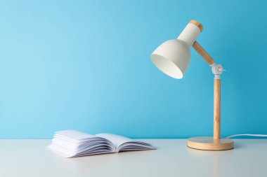 Okul temalı kurulum, açık günlük ve esnek lamba gibi masa ögelerini gösteriyor. Mavi duvar arkaplanı, metin veya reklam için alan sunar