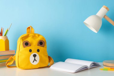 Kırtasiye malzemeleri, kitaplar, açık günlük, lamba ve sevimli sırt çantasının olduğu düzenli bir okul masasının yan görüntüsü. Eğitim içeriği ya da duyurular için harika