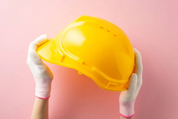 Tribute to hardworking women on Labor Day. First person top view of woman\'s gloved hands with safety helmet on pink backdrop. Advertise here