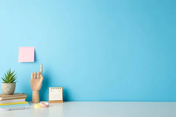 stock image Capture attention with side view composition of a student's workplace, featuring a white desk, notepads,wooden hand and stationery against a blue backdrop, offering ample space for text or ads