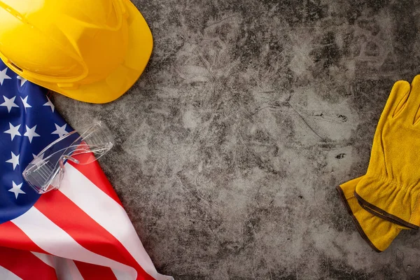 Amerikan İşçi Bayramı 'nda inşaat işçilerinin paha biçilmez katkılarını takdir etmek. Bayrak, kask ve eldivenlerin üzerinde grunge desenli gri beton zemin. Reklam veya metin için ideal