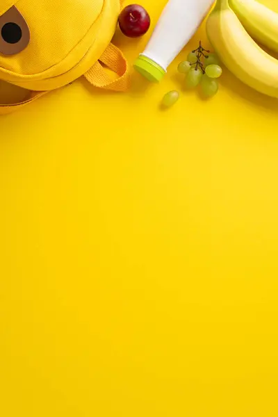 自然食品 バナナ ブドウ プラム ヨーグルトのボトル テキストや広告のためのスペースを持つ黄色の背景の面白いバックパックの垂直トップビューで健康的な習慣を奨励 — ストック写真