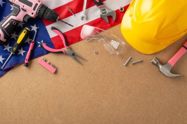 İşçi Bayramı 'nda kadın işçilerin ruhunu kucaklamak. Ahşap izole arka planda bir Amerikan bayrağı ve pembe inşaat araçlarının üst görünümü, reklamlar veya metin yerleştirme için yer sağlar