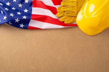 İşçi Bayramı anma konsepti. Amerikan bayrağının üst görüntüsü, işçi donanımı, güvenlik eldivenleri ve inşaat miğferi Amerikan işçilerinin sıkı çalışma ve adanmışlığını simgeliyor, metin veya reklam için boş alan