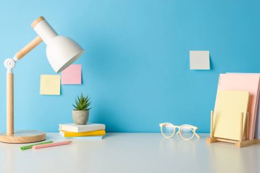 Okul malzemeleri, kitaplar, gözlükler, kalemler, saksı ve lamba ile yan görüntülerde eğitim çalışma alanı sergilendi. Metin veya reklamlar için yapışkan notlar içeren mavi duvar arkaplanı