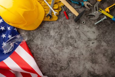 İşçi Bayramı 'nda inşaat işçilerinin adanmışlık ve becerilerini onurlandırmak. Üzerinde bayrak, kask, eldiven ve grunge desenli gri beton üzerindeki aletlerin olduğu bir fotoğraf. Reklamlar ya da metinler için kopyalama alanı