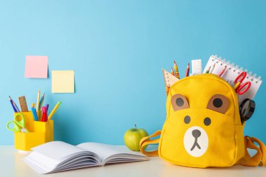 Atmosfer öğreniyorum. İyi hazırlanmış bir masanın yan görüntüsü - kalem standı, cetvel, kitap, not defteri ve daha fazlası. Bir oyuncak ayı okul çantası ve elma mavi duvara karşı okul temalı ortamı güçlendirir.