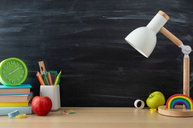 Öğrenci işyeri düzeniyle verimli bir çalışma için zemin hazırlayın. Yandan görüntü sunumu lamba, kırtasiye ve ahşap masadaki kitaplar karatahta izole arkaplan, metin veya reklam alanı ile