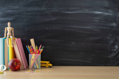 School supplies layout. Side view photo of desk setup with pencils organizer, ruler, books, red apple, mannequin body, and more on chalkboard background. Great for educational content or advertising clipart