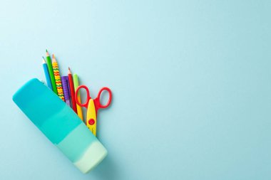 Derli toplu bir masadaki okula dönüş gereksinimleri: renkli kalemler, kalemler, makaslar ile kalem kılıfının üst görünümü, hepsi metin veya promosyonlar için geniş bir pastel mavi arka plan üzerinde