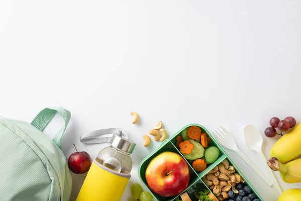 A nourishing school break captured from above, featuring a lunchbox filled with sandwiches accompanied by bottle, nuts, berries and rucksack on a white isolated backdrop, ready for text or advertising