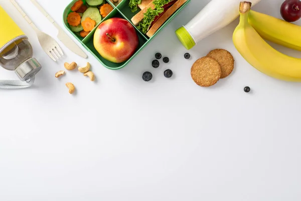An inviting and nutritious school break arrangement displayed from a bird\'s eye top view. A lunchbox containing delicious sandwiches set against a white backdrop with space for text or advertising