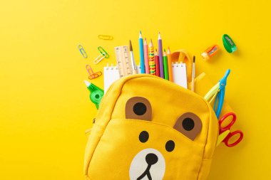Sarı izole edilmiş arka planda şirin bir çocuk çantasında çeşitli renkli okul malzemelerini gösteren bir fotoğraf ile eğlenceli öğrenme ruhunu serbest bırakın. Mesaj veya reklam için mükemmel.