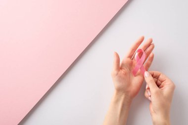 Bu Uluslararası Göğüs Kanseri Farkındalığı Ayı 'na katılın. Üst görüntüde iki parçalı pembe ve beyaz arka planda pembe kurdele tutan kadın elleri resmi var. Mesaj veya reklam için yer var.