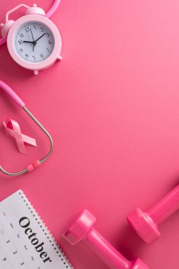 Göğüs kanseri farkındalığı semineri. Ekim aylı takvimin dikey üst görünümü, pembe kurdele işareti, steteskop, kız gibi halterler, çalar saat, pembe arka planda reklam için boş alan.