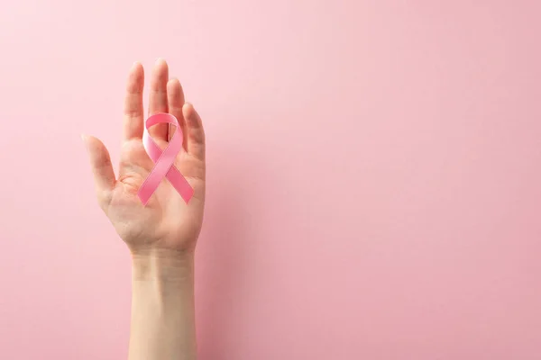 Raise your voice this International Breast Cancer Awareness Month. Top view photo of woman\'s hands holding a pink ribbon on pastel pink backdrop, offering copyspace for text or advertising