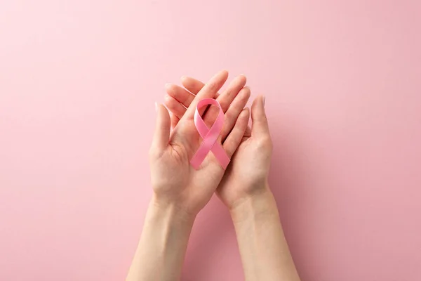 Stand together for International Breast Cancer Awareness Month. Top view of female hands with pink ribbon on pastel pink isolated background, providing copyspace for text or ad including