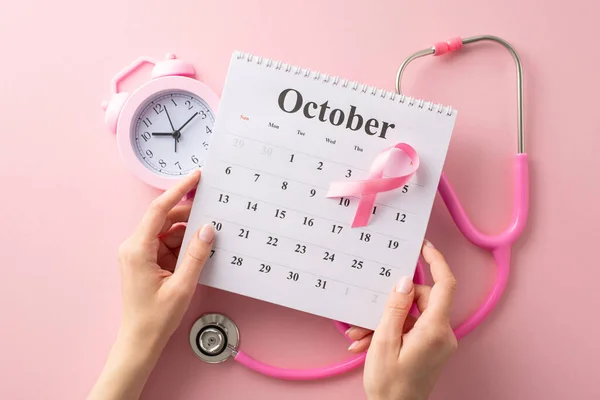 Raise your voice this World Breast Cancer Awareness Month. Top view photo of hands holding calendar and pink ribbon, stethoscope and clock on pink backdrop, offering copyspace for text or advertising