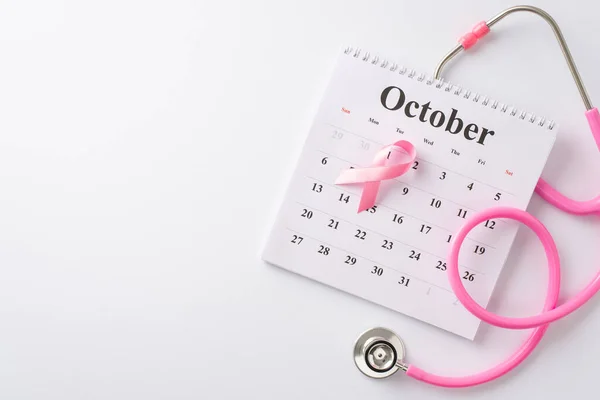 Empower the fight against breast cancer during International Breast Cancer Awareness Month. Top view image of calendar, stethoscope and pink ribbon on white background, ideal for text or advertising