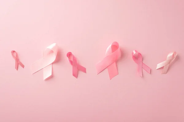 Breast cancer support concept. Top view of pink ribbon signs on pastel pink background, perfect for advertising or text placement