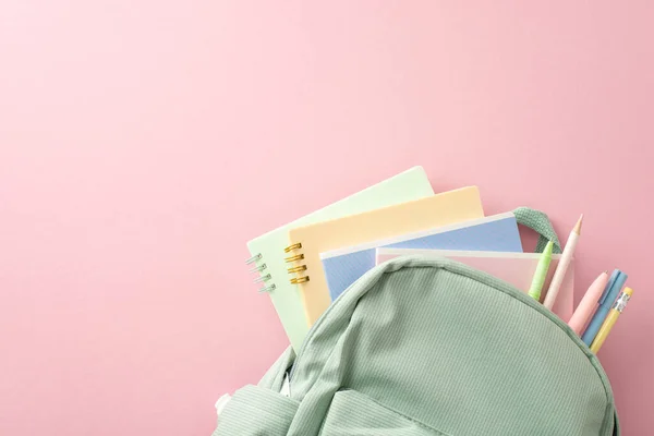 Top view image featuring school or college essentials: pastel backpack with pens, pencils, and colorful copybooks on pink backdrop. Ad space available