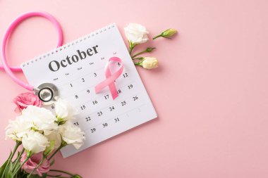 Erken teşhis kampanyası. Ekim takviminin en üst görüntüsü steteskop, pembe kurdele ve pastel pembe arkaplan üzerinde yumuşak östoma çiçekleri, bilgilendirici metin veya reklamlar için yer sağlar
