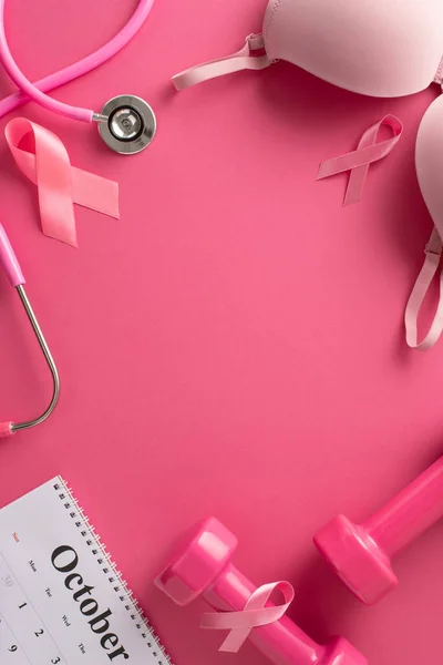 Breast cancer research funding. Vertical top view of calendar, pink ribbon symbols, stethoscope, brassiere, feminine dumbbells on pink background with empty frame for text or advertising