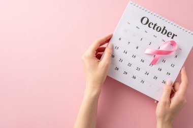Uluslararası Göğüs Kanseri Farkındalığı Ayı boyunca desteğinizi gösterin. El, takvim ve pembe kurdeleli üst görünüm resim pastel pembe izole arka plan, metin veya reklam için uygun