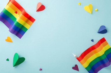 Temmuzda LGBTQ + Gurur Ayı 'nı canlı gurur bayrakları ve gökkuşağı kalpleriyle anmak. Yukarıdan yakalanan yumuşak açık mavi izole arkaplan, reklamlar veya metin yerleştirme için idealdir