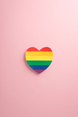 LGBTQ + Gurur Ayı şenliklerine dalın. Büyüleyici dikey yukarıdan aşağıya yakalama görüntüsüne tanık olun. LGBTQ + bayrağı kalp şeklinde, yumuşak pastel pembe arka planda. Telif alanı sağlanan reklam dosyasıName