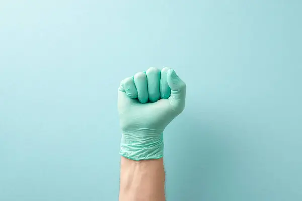 Necessity of regular medical check-ups concept. High angle view picture of doctor\'s hand in fist in sterilized glove on teal background with copy-space for text or promotional messages