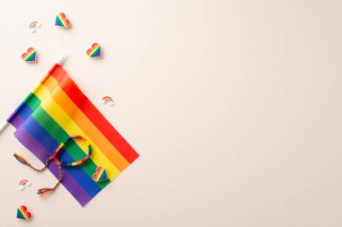 Flat lay of celebration LGBT parade with rainbow flag, pin badges, decorative hearts and wristband with empty space for text on beige background clipart