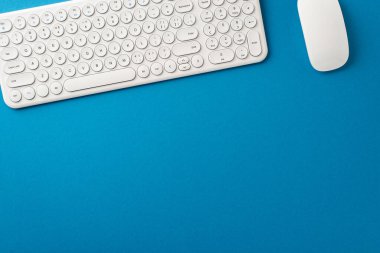 Modern Office Essentials: Beyaz klavyeli üst görünüm kompozisyonu ve mavi yüzeyli kablosuz fare. Metin veya reklamlar için boş alan