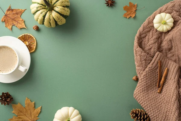 Embrace autumn aesthetic. High-angle top view featuring warm brown sweater, steaming coffee, pattypans, acorns, cinnamon, maple leaves, pine cones, dried orange slice on green surface, space for text