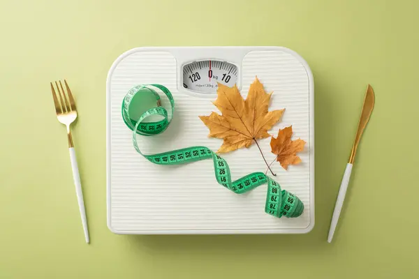 Fall fitness journey: Top view featuring scale, tape measure, cutlery, maple leaves on green surface. Image perfect for promotions or advertisements