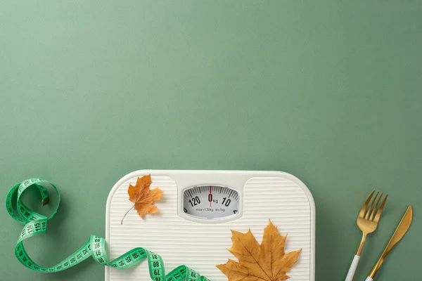 Fall season fitness plan. Top view shot displaying scale, tape measure, fork, knife, maple leaves on green background. Customize with text or promotional material