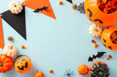 Çocukların Cadılar Bayramı şeker avının mucizesini kucaklayın. Şekerler ve cadılar bayramı süslemeleriyle dolu balkabağı sepetinin yüksek açılı fotoğrafı mavi izole bir zemin üzerinde, metin veya reklam yerleştirme için mükemmel.