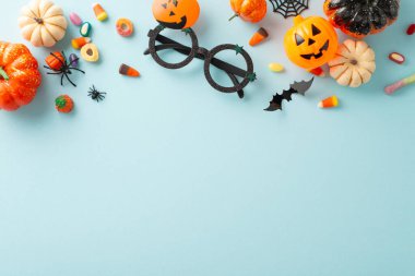 Cadılar Bayramı 'nda şeker mi şaka mı oyunu. Tematik dekorun üst görüntüsü: küçük balkabakları, jöle şekerlemeleri, ürkütücü örümcekler, ağ, yarasa ve soluk mavi yüzeyde parti gözlükleri. Mesajlar ve terfiler için mükemmel