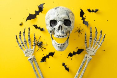 Cadılar Bayramı gecesinin ürkünç havasını benimse. Sarı yalıtılmış arka planda insan kafatası ve elleri ve konfetilerin üst görüntüsü, metin veya reklam içeriği için yer sunuyor