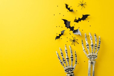 Cadılar Bayramı 'nın gece korkularına dalmak. Sarı yalıtılmış bir yüzey üzerinde örümceklerle, kağıt yarasalarla ve konfetilerle dolu bir iskelet görüntüsü. Metin veya reklam için mükemmel.