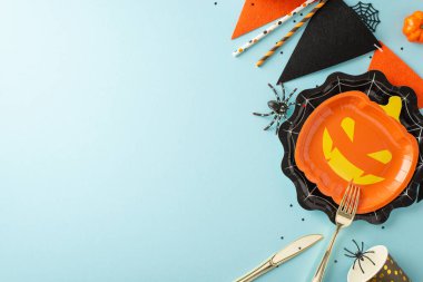 Eşsiz Cadılar Bayramı yemek sahnesi. Komik balkabağı & örümcek ağı tabakları, çatal bıçaklar, tek kullanımlık bardaklar, pipetler, balkabağı, ürkütücü örümcekler, çelenkler, yumuşak mavi arkaplan üzerinde konfeti, metin alanı dahil