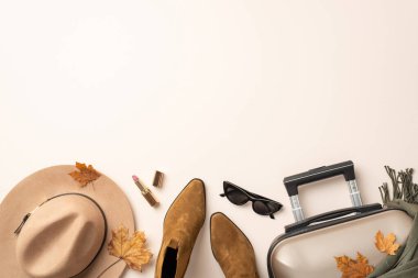 Bir sonbahar macerası için hazırlanmak - kadın seyahat takımlarının üst görünümü: keçeli şapka, kedi gözü güneş gözlükleri, eşarp, ayak bileği çizmeleri, bavul, ruj, tarafsız bir arkaplanda düşmüş akçaağaç yaprakları