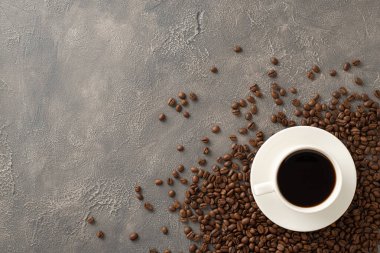 Aromatik Uyanış: Kahve günü konsepti, kahve çekirdekleri ve kahve fincanının en üst görüntüsüne sahip koyu gri grunge tuval ile boş uzay tuvaline karşı düzenlenmiş.